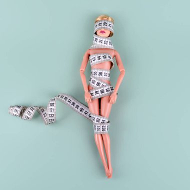 Ölçüm bandına sarılı oyuncak bebek. Tanınmayan plastik bebek, kilo kaybı, perhiz ve zayıflama, diyet, iştahsızlık, aşırı yeme kontrolü, mükemmel vücut konsepti için kadın kavgası. Boş telif alanı