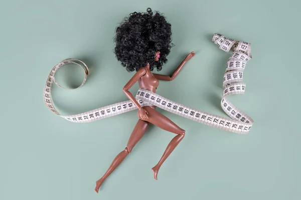 Doll wrapped in measuring tape. Tied up unrecognizable plastic doll, weight loss, fasting and slimming, diet, anorexia, overeating control, female fight for perfect fit body concept. — Stock Photo, Image
