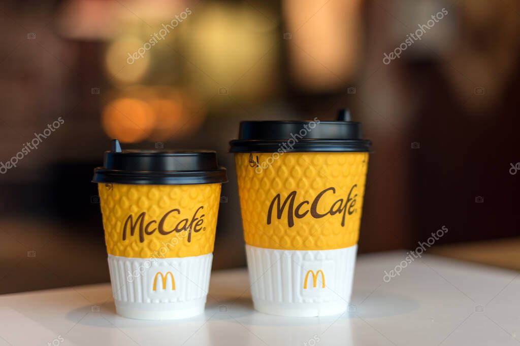 Kyiv, Ukraine - OCTOBER 12, 2020: Two paper cups of coffee with McDonald's and McCafe logo on table near window on background of blurred McDonald's restaurant. Selective focus.