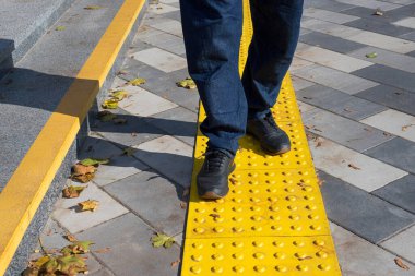 Sarı bloklarda yürüyen bir adam kör engelliler için kaldırım döşemesi. Braille blokları, görme engelliler için dokunsal fayanslar, Tenji blokları. Kaldırımlarda, merdivenlerde desenli yer göstergeleri.