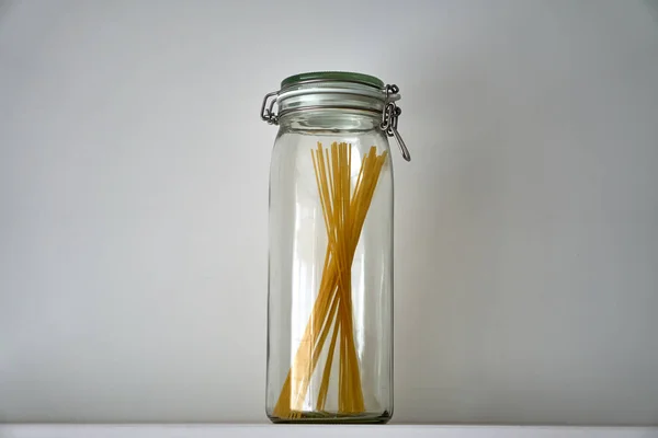 Glass jars with lid for food on white shelf. Storage kitchen. Pasta, spaghetti.