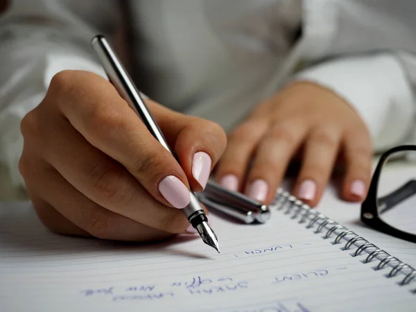 Woman in a White Long Sleeved Shirt Holding a Pen and Writing on a Paper