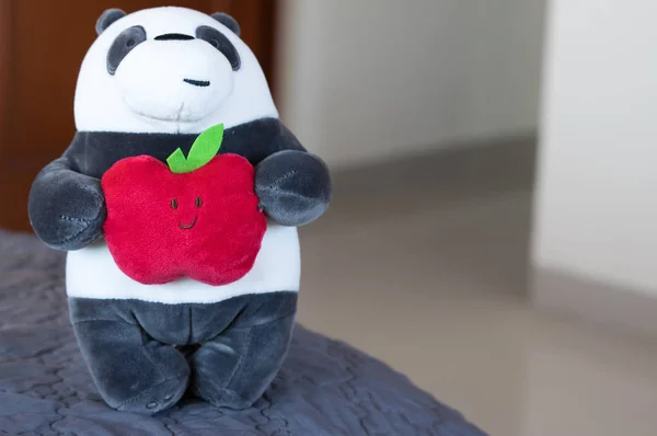 Panda plush toy holding a red apple with a happy face.