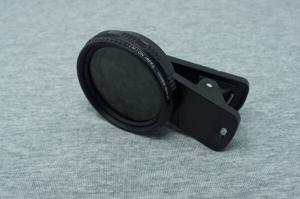 Variable neutral density filter with clip for smartphones. Fabric, grey background.