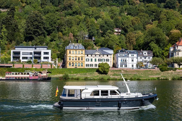 View of residential buildings. Houses on the river bank. A boat floats past the townhouses on the water. There are many beautiful green trees around. Modern area near the historic city of Heidelberg.
