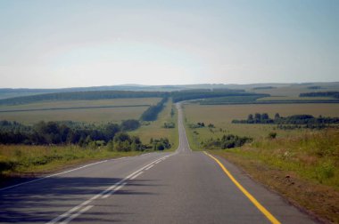 İlginç bir manzara. Yol ufkun ötesindeki mesafeye gidiyor. Tarlalar ve ormanlar arasındaki yol.