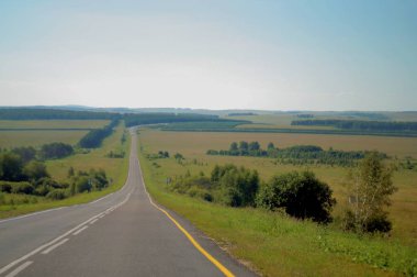 İlginç bir manzara. Yol ufkun ötesindeki mesafeye gidiyor. Tarlalar ve ormanlar arasındaki yol.
