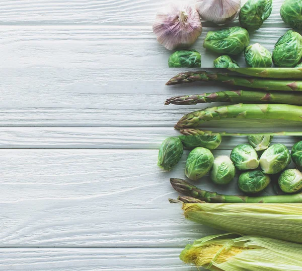 Colagem de couves-de-bruxelas verdes maduras, espargos, milho e alho sobre mesa de madeira branca — Fotografia de Stock