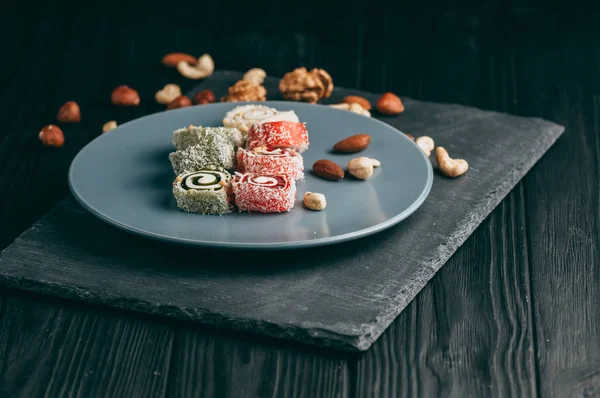 Traditional oriental sweets and nuts: hazelnuts, cashews on a dark wooden background. Turkish dessert is the Rakhat locus. View from above. Place under the text