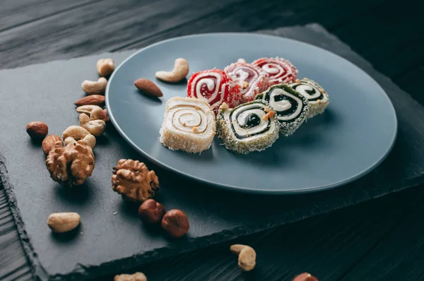 Traditional oriental sweets and nuts: hazelnuts, cashews on a dark wooden background. Turkish dessert is the Rakhat locus. View from above. Place under the text