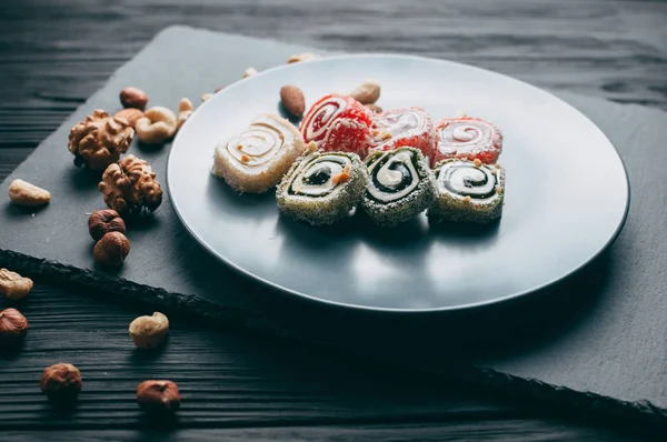 Traditional oriental sweets and nuts: hazelnuts, cashews on a dark wooden background. Turkish dessert is the Rakhat locus. View from above. Place under the text