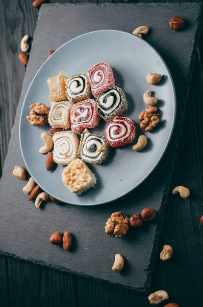 Traditional oriental sweets and nuts: hazelnuts, cashews on a dark wooden background. Turkish dessert is the Rakhat locus. View from above. Place under the text