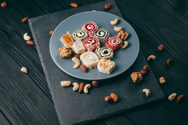 Traditional oriental sweets and nuts: hazelnuts, cashews on a dark wooden background. Turkish dessert is the Rakhat locus. View from above. Place under the text