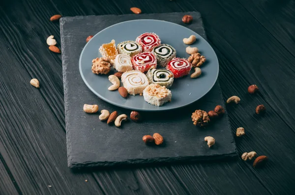 Traditional oriental sweets and nuts: hazelnuts, cashews on a dark wooden background. Turkish dessert is the Rakhat locus. View from above. Place under the text