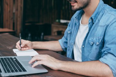Erkekler ellerini ücretsiz Wi-Fi, bir defter ön planda bir kafede ahşap bir kahverengi masa üstünde a laptop basılır. Bir çevirmen için kavram zaman, her yerde çalışır. Yan görünüm, kavram