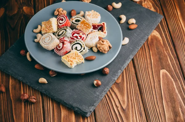 Traditional oriental sweets and nuts: hazelnuts, cashews on a brown wooden background. Turkish dessert is the locus of Rahat. View from above. Place under the text