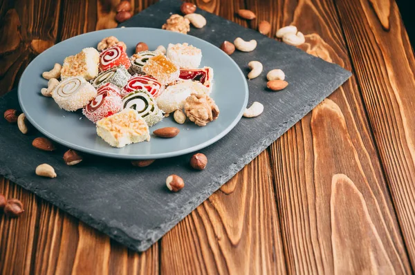 Traditional oriental sweets and nuts: hazelnuts, cashews on a brown wooden background. Turkish dessert is the locus of Rahat. View from above. Place under the text