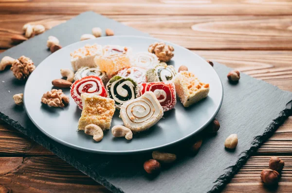 Traditional oriental sweets and nuts: hazelnuts, cashews on a brown wooden background. Turkish dessert is the locus of Rahat. View from above. Place under the text