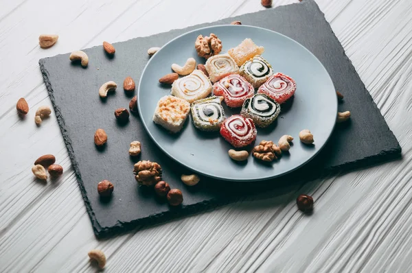 Traditional oriental sweets and nuts: hazelnuts, cashews on a white wooden background. Turkish dessert is the locus of Rahat. View from above. Place under the text