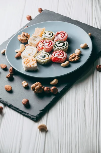 Traditional oriental sweets and nuts: hazelnuts, cashews on a white wooden background. Turkish dessert is the locus of Rahat. View from above. Place under the text