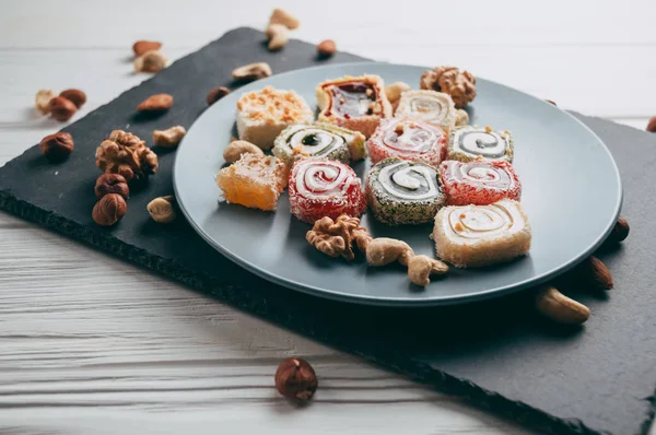 Traditional oriental sweets and nuts: hazelnuts, cashews on a white wooden background. Turkish dessert is the locus of Rahat. View from above. Place under the text