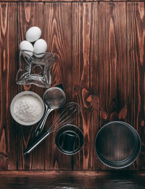 Maddeler de yalan çırpma teli tam un için üç tavuk yumurtası ve kayrak Sedye nerede yemeklerinde ahşap bir kahverengi masa üzerinde. Yukarıdan görüntüleyin. Metnin altında yer