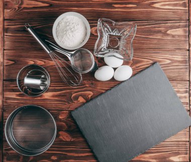 Maddeler de yalan çırpma teli tam un için üç tavuk yumurtası ve kayrak Sedye nerede yemeklerinde ahşap bir kahverengi masa üzerinde. Yukarıdan görüntüleyin. Metnin altında yer