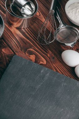 Maddeler de yalan çırpma teli tam un için üç tavuk yumurtası ve kayrak Sedye nerede yemeklerinde ahşap bir kahverengi masa üzerinde. Yukarıdan görüntüleyin. Metnin altında yer