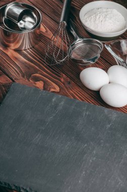 Maddeler de yalan çırpma teli tam un için üç tavuk yumurtası ve kayrak Sedye nerede yemeklerinde ahşap bir kahverengi masa üzerinde. Yukarıdan görüntüleyin. Metnin altında yer