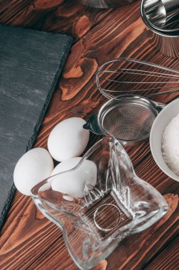 Maddeler de yalan çırpma teli tam un için üç tavuk yumurtası ve kayrak Sedye nerede yemeklerinde ahşap bir kahverengi masa üzerinde. Yukarıdan görüntüleyin. Metnin altında yer