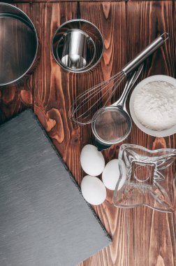 Maddeler de yalan çırpma teli tam un için üç tavuk yumurtası ve kayrak Sedye nerede yemeklerinde ahşap bir kahverengi masa üzerinde. Yukarıdan görüntüleyin. Metnin altında yer