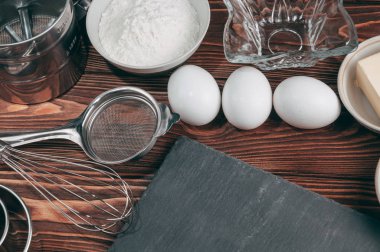 Maddeler de yalan çırpma teli tam un için üç tavuk yumurtası ve kayrak Sedye nerede yemeklerinde ahşap bir kahverengi masa üzerinde. Yukarıdan görüntüleyin. Metnin altında yer