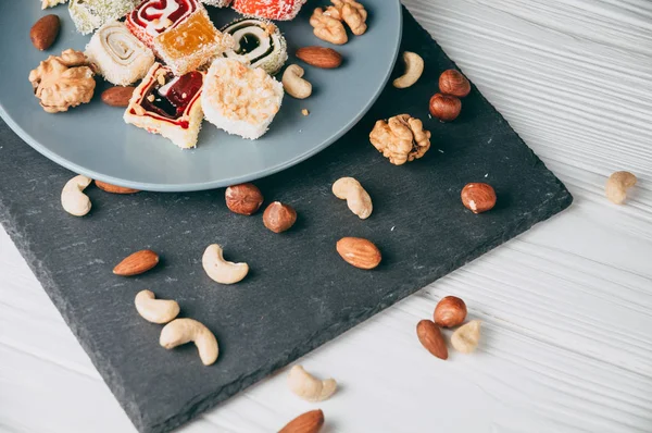 Traditional oriental sweets and nuts: hazelnuts, cashews on a white wooden background. Turkish dessert is the locus of Rahat. View from above. Place under the text