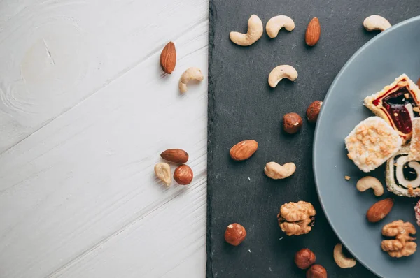 Traditional oriental sweets and nuts: hazelnuts, cashews on a white wooden background. Turkish dessert is the locus of Rahat. View from above. Place under the text