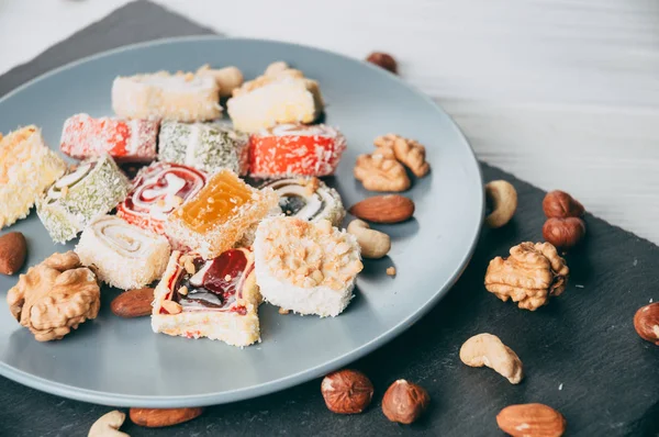 Traditional oriental sweets and nuts: hazelnuts, cashews on a white wooden background. Turkish dessert is the locus of Rahat. View from above. Place under the text