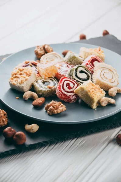 Traditional oriental sweets and nuts: hazelnuts, cashews on a white wooden background. Turkish dessert is the locus of Rahat. View from above. Place under the text