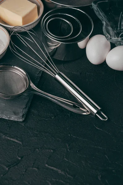 Ingredients and dishes on a black concrete table, where the corolla also lies, is filled with flour, three chicken eggs and a slate board. View from above. Place under the text