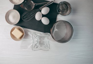 Malzemeler ve yemekleri de bir corolla içerir, beyaz bir ahşap masa üzerinde un, üç tavuk yumurtası ve kayrak bir yönetim kurulu ile doldurulur. Yukarıdan görüntüleyin. Metnin altında yer