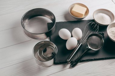 Malzemeler ve yemekleri de bir corolla içerir, beyaz bir ahşap masa üzerinde un, üç tavuk yumurtası ve kayrak bir yönetim kurulu ile doldurulur. Yukarıdan görüntüleyin. Metnin altında yer