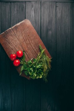 Domates, maydanoz ve dereotu bir ahşap kesme tahtası siyah ahşap zemin üzerinde. Görünüm sperm hücrelerinin altında metin yerleştirin