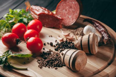 Siyah bir tablo ve bir kahverengi tahta üzerinde füme salam. Biberiye, sarımsak ve biber ve domates kiraz, dereotu, maydanoz ile sosis