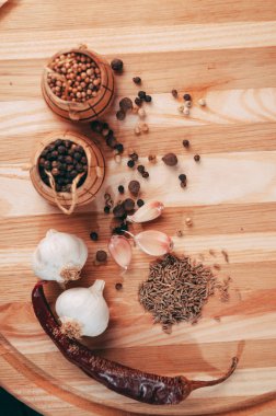 Baharatlar: kırmızı biber, kara biber, sarımsak, kimyon, kişniş, tatlı biber yalan bir kahverengi ahşap tahta siyah bir tablo üzerinde yuvarlak. Metnin altında yer