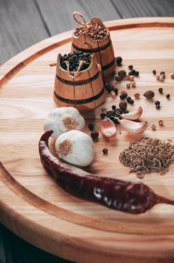 Baharatlar: kırmızı biber, kara biber, sarımsak, kimyon, kişniş, tatlı biber yalan bir kahverengi ahşap tahta siyah bir tablo üzerinde yuvarlak. Metnin altında yer