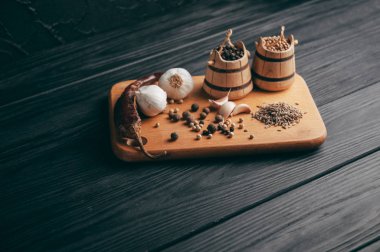 Baharatlar: kırmızı biber, kara biber, sarımsak, kimyon, kişniş, tatlı biber yalan bir kahverengi ahşap tahta üzerinde siyah bir tablo üzerine. Metnin altında yer