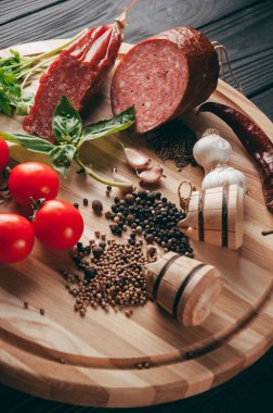 Siyah bir tablo ve bir kahverengi tahta üzerinde füme salam. Biberiye, sarımsak ve biber ve domates kiraz, dereotu, maydanoz ile sosis