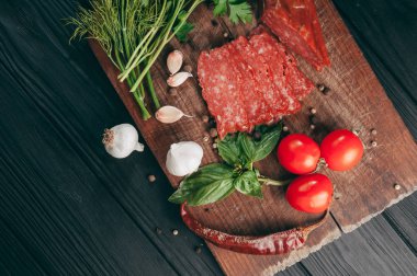 Siyah bir tablo ve bir kahverengi tahta üzerinde füme salam. Biberiye, sarımsak ve biber ve domates kiraz, dereotu, maydanoz ile sosis.