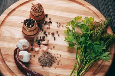 Baharatlar: kırmızı biber, kara biber, sarımsak, kimyon, kişniş, tatlı biber yalan bir kahverengi ahşap tahta siyah bir tablo üzerinde yuvarlak. Metnin altında yer