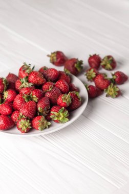 Beyaz ahşap zemin üzerinde bir tabak içinde taze çilek