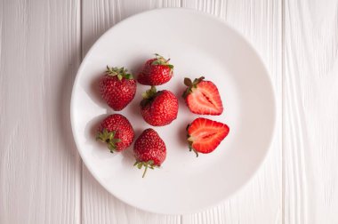 Beyaz ahşap zemin üzerinde bir tabak içinde taze çilek