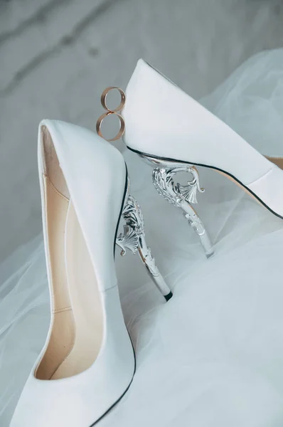A pair of white wedding shoes with rings on a stool